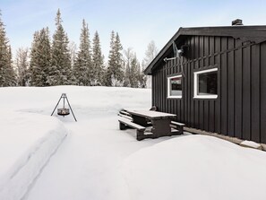 Una cabaña con fachada de madera, una mesa de picnic y un pozo de fuego en la nieve.