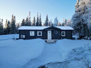 Una cabaña de un piso con techo nevado, rodeada de un bosque.