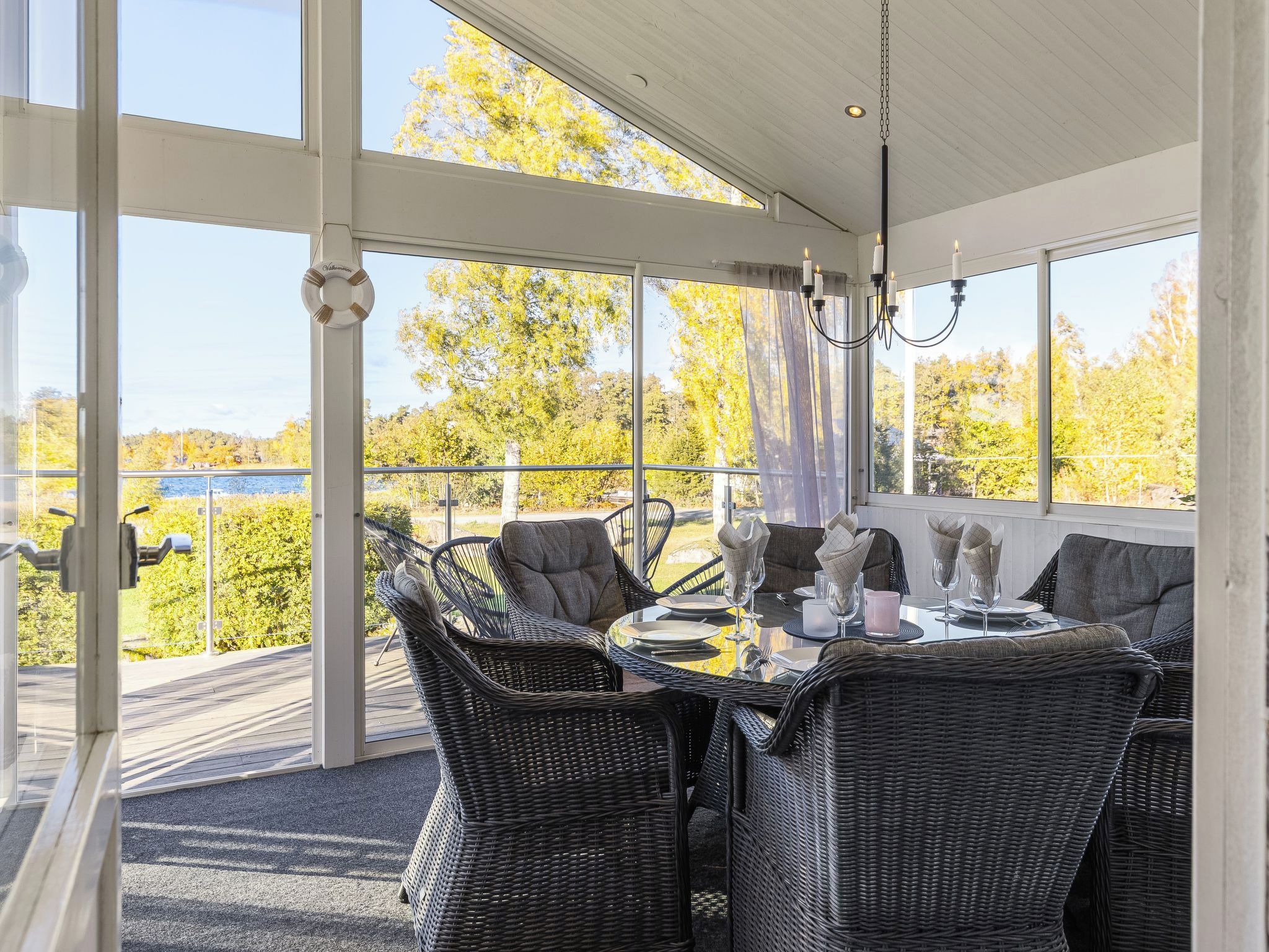 Een overdekt terras met rieten meubilair, een gedekte tafel voor twee personen en uitzicht op bomen en water.