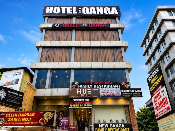 Ein mehrstöckiges Gebäude mit Schildern für das Hotel New Ganga, ein Familienrestaurant und eine Zahnarztpraxis.