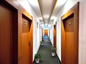 Un pasillo de hotel con puertas de madera, números de habitación y plantas en macetas.