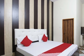 Un dormitorio con cama blanca, almohadas rojas y pared a rayas.