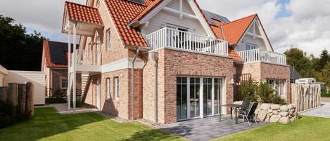 A two-story house with a red-tiled roof, a balcony, and a patio area.