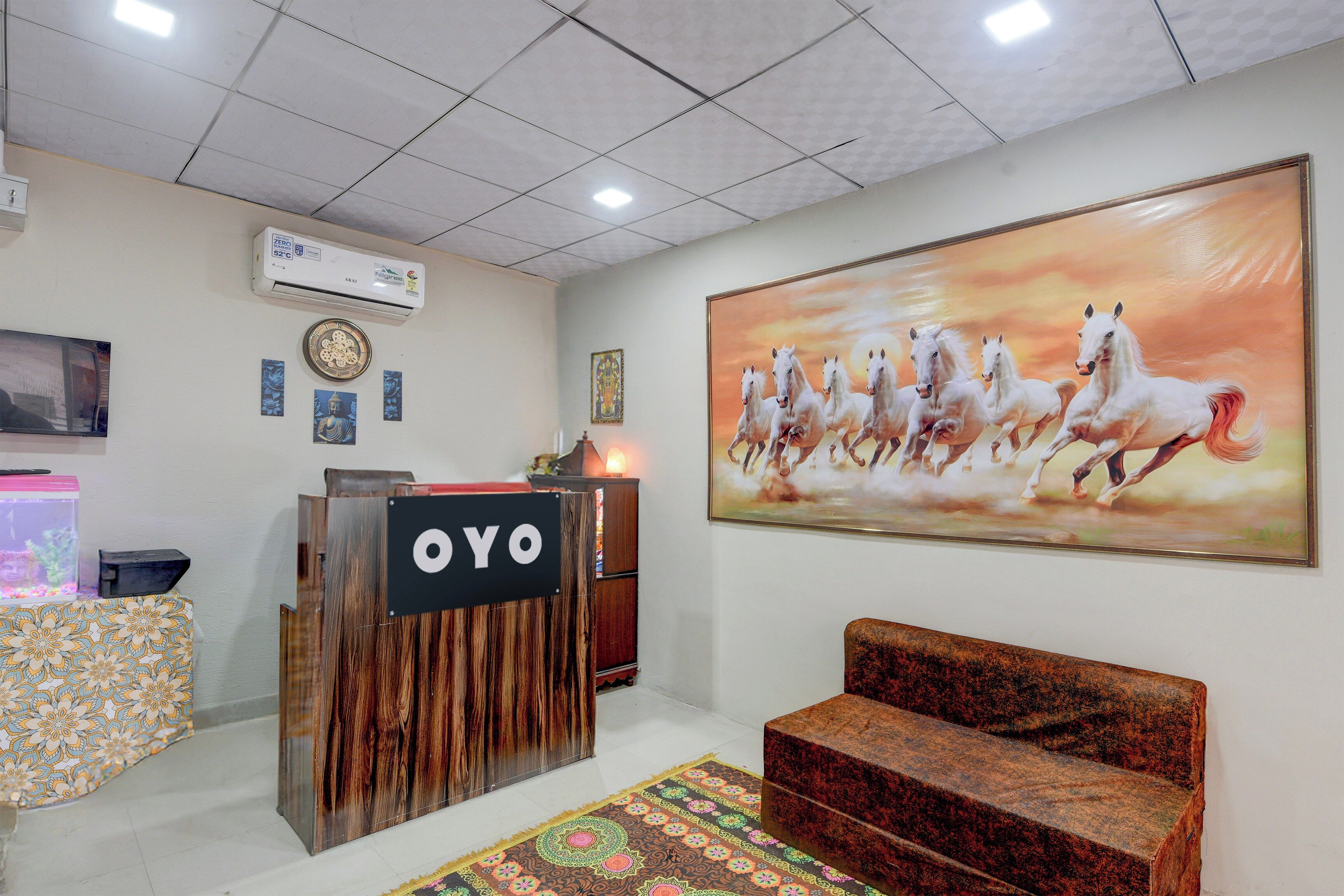 A reception area with a wooden reception desk, a large painting of horses, a clock, and a wall-mounted air conditioner.