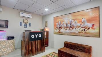 A reception area with a wooden reception desk, a large painting of horses, a clock, and a wall-mounted air conditioner.