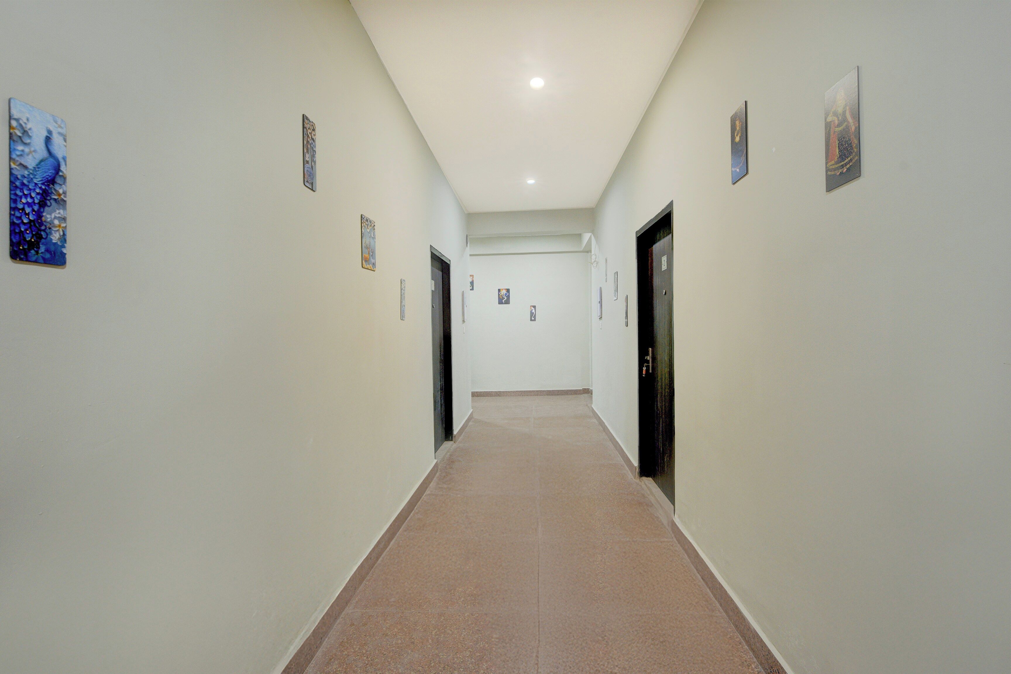 A corridor with doors on both sides, a tiled floor, and small artwork on the walls.