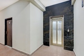 A hallway with a wooden door marked with the number 1, a marble wall, and an elevator with a control panel. - Hotel O Regal Garden (Faridabad)