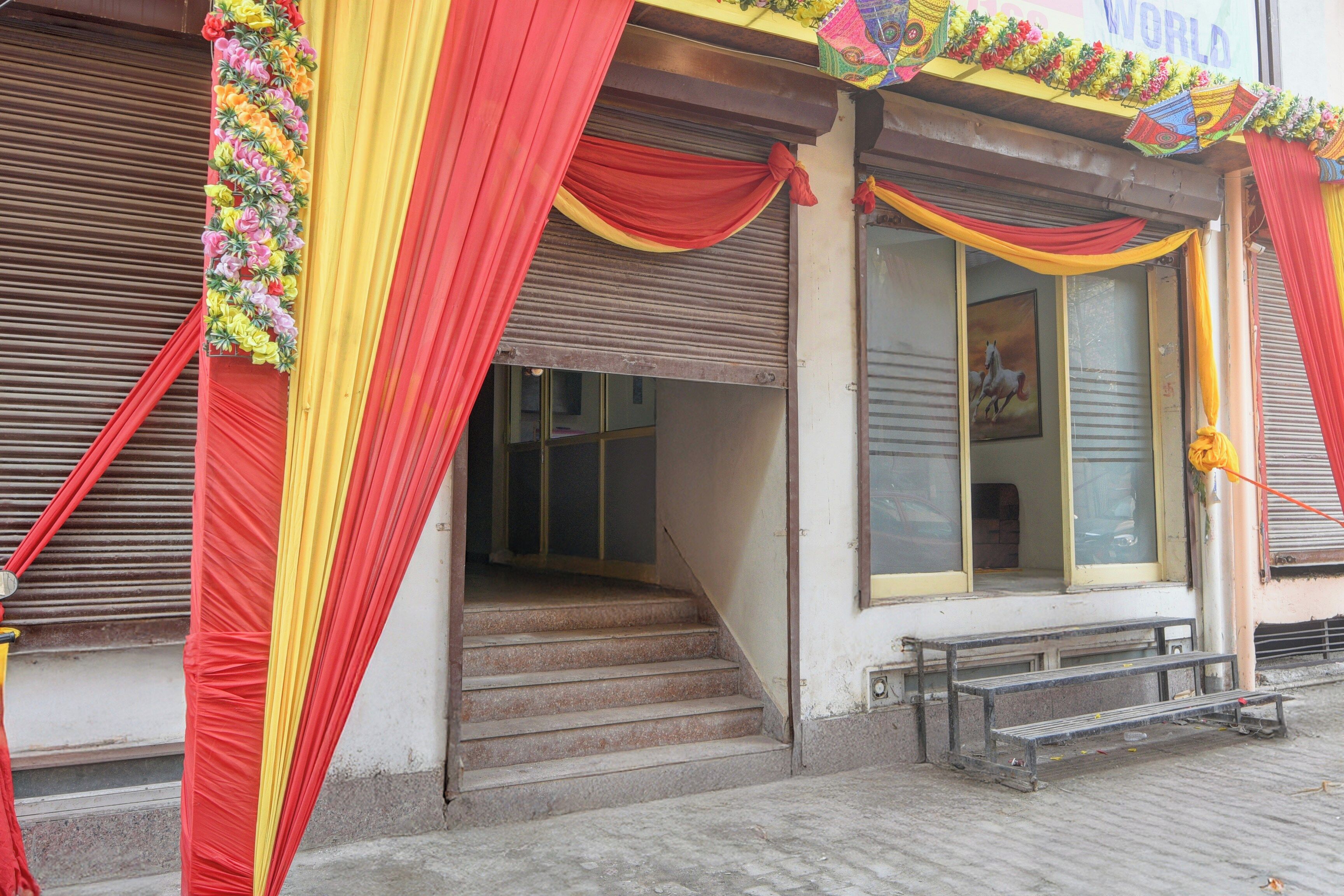 A building with a closed shutter, a staircase leading to the entrance, and a bench outside.