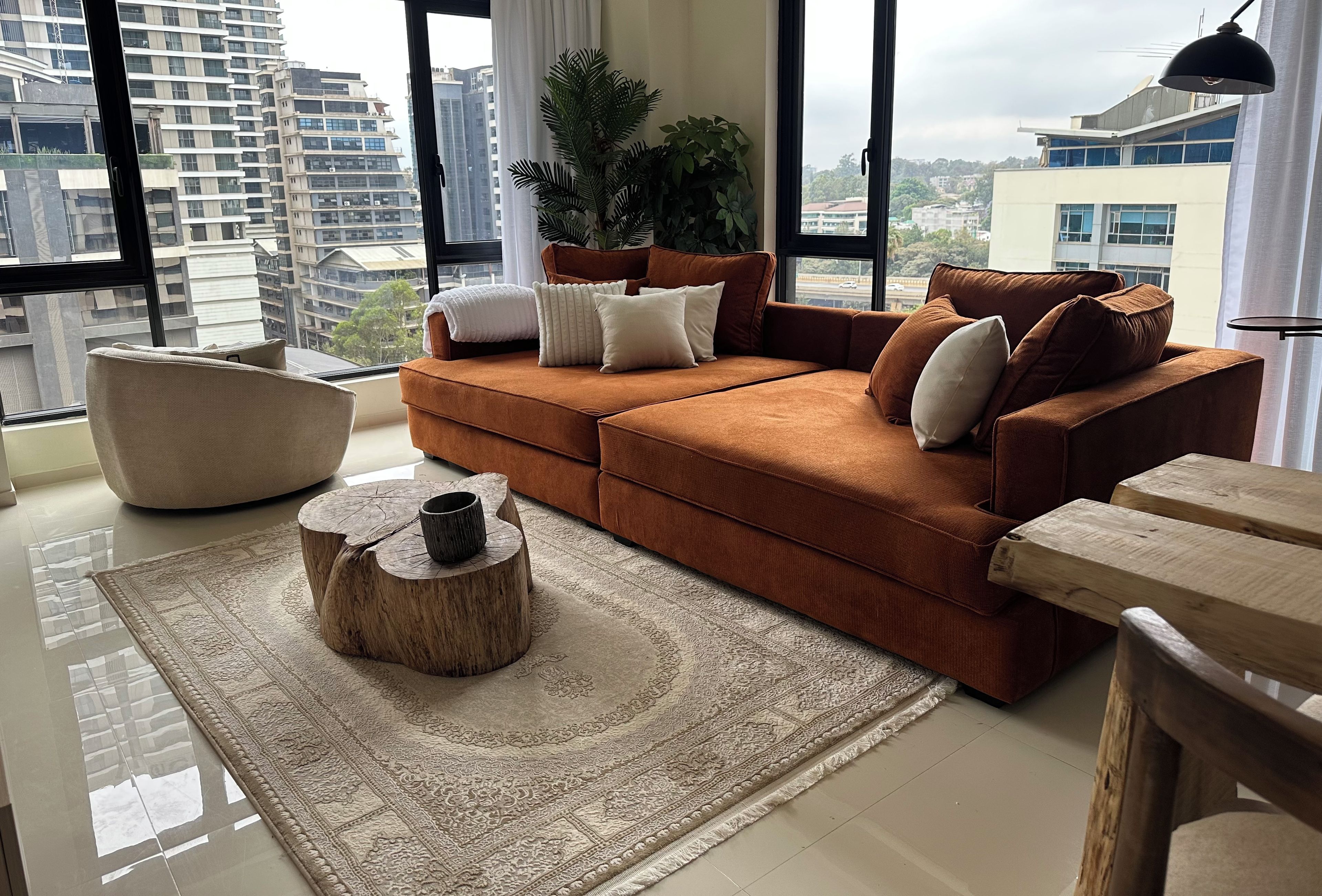 A modern living room with a brown sofa, a round wooden coffee table, and a large window offering a city view.