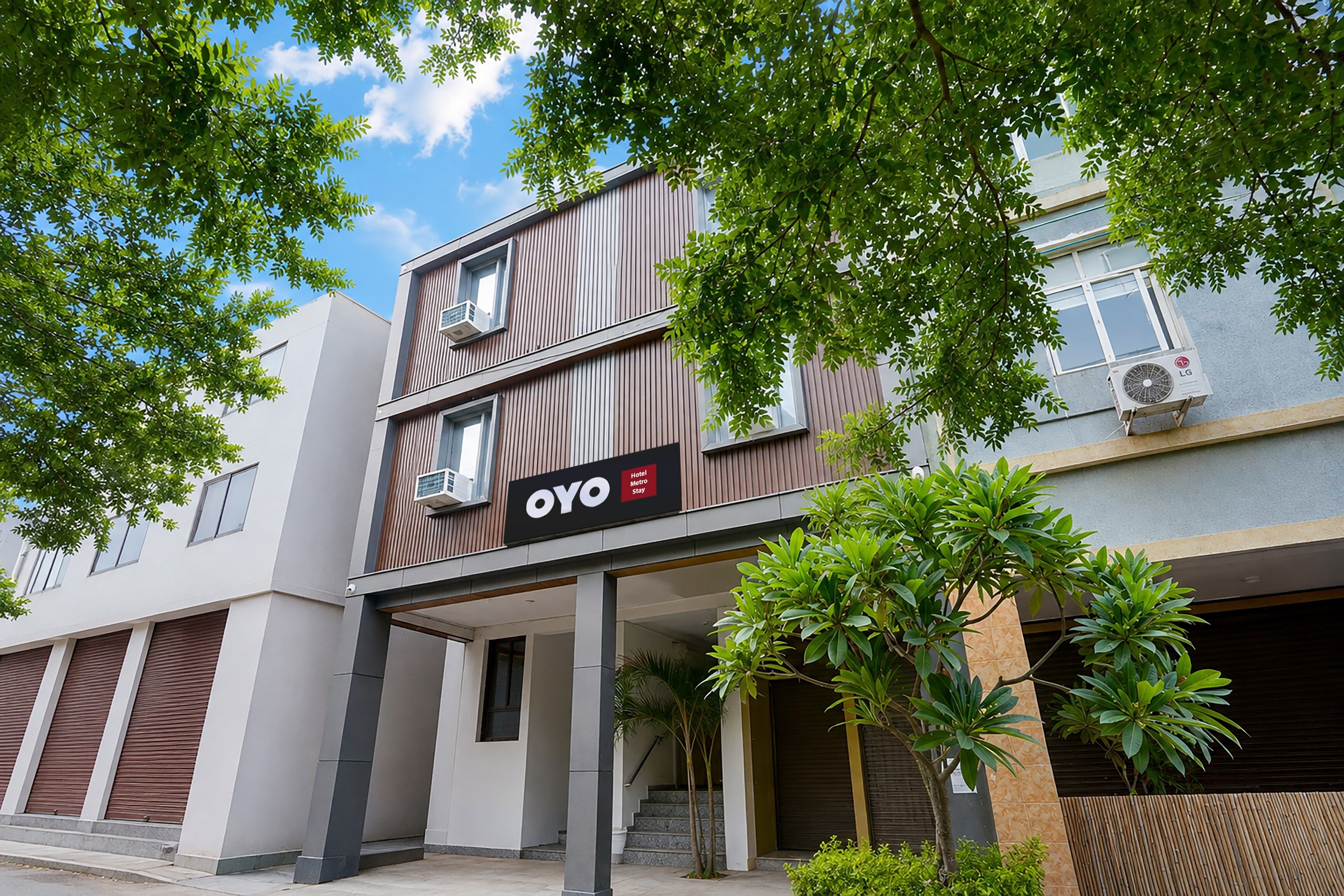 A modern hotel building with a prominent OYO logo, air conditioning units, and a covered entrance area with steps.