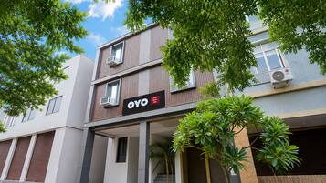 A modern hotel building with a prominent OYO logo, air conditioning units, and a covered entrance area with steps.