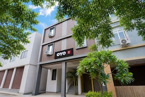 Un moderno edificio de hotel con un llamativo logotipo de OYO, unidades de aire acondicionado y un área de entrada cubierta con escalones.