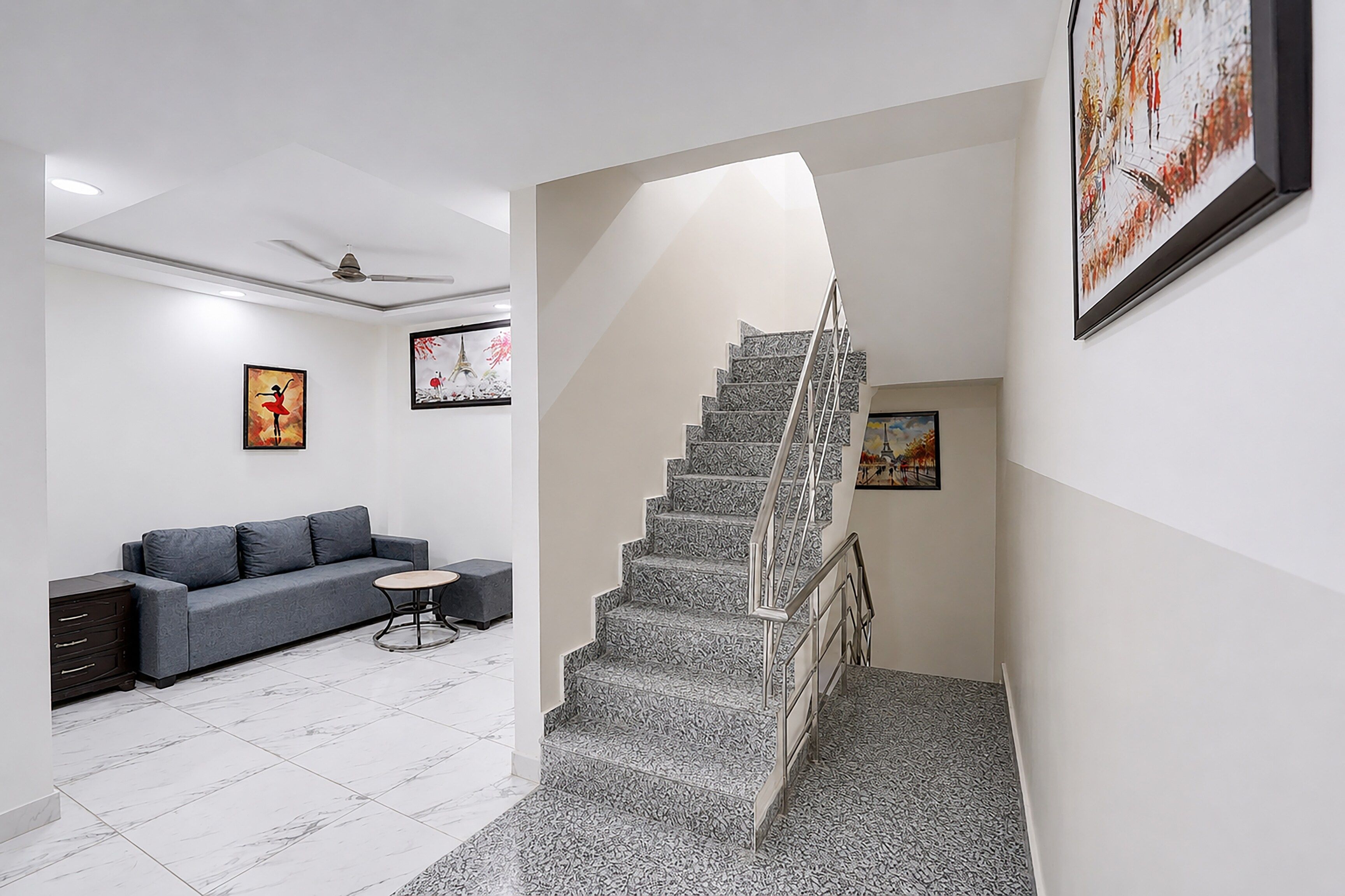 A modern interior with a grey sofa, a small round table, and a staircase with a metal railing.
