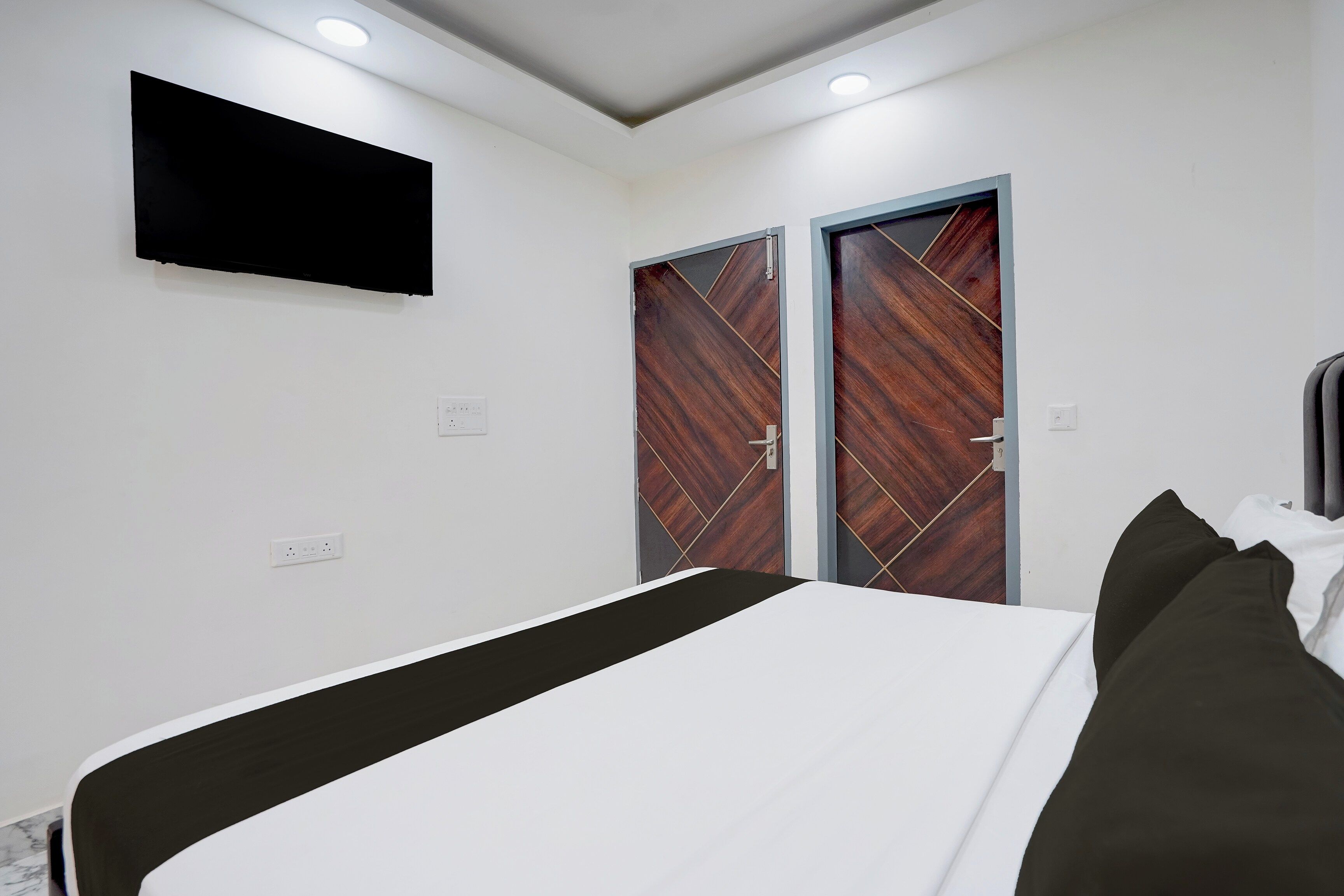 A bedroom with a bed, a flat-screen TV mounted on the wall, and two doors with a geometric pattern.