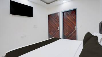 A bedroom with a bed, a flat-screen TV mounted on the wall, and two doors with a geometric pattern.