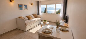 A cozy room with a sofa, a dining table set for two, and a view of a lake. - New Listing (Saint-Florent)