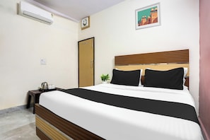 A hotel room with a bed, a bedside table with a kettle and cups, a wall-mounted air conditioner, a door, and a framed picture on the wall. - Hotel O Royal Stay (Faridabad)