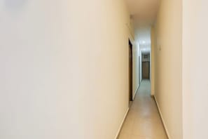 A narrow, well-lit hallway with plain walls and a tiled floor, leading to a door at the end. - Hotel O Royal Stay (Faridabad)