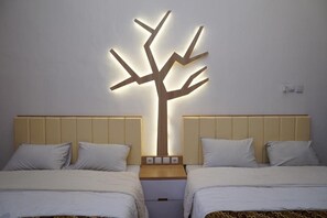 Quarto de hotel com duas camas, luminária fixada na parede em formato de árvore e mesa de cabeceira de madeira entre as camas.