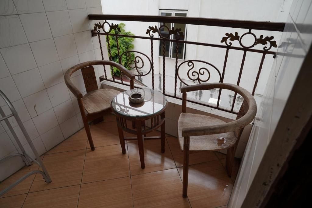 A small balcony with two wooden chairs and a round table, featuring a metal railing with decorative elements.