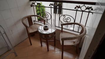 A small balcony with two wooden chairs and a round table, featuring a metal railing with decorative elements.