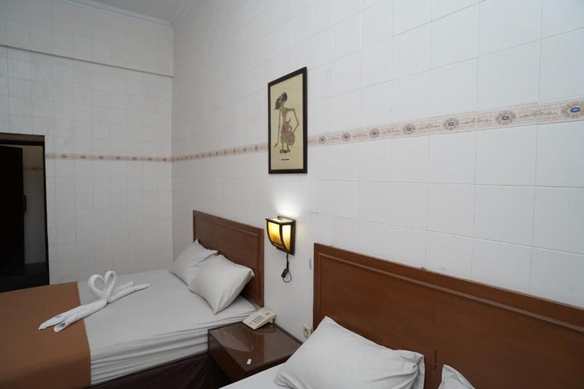 Quarto de hotel com duas camas, uma luminária fixada na parede e um quadro emoldurado.