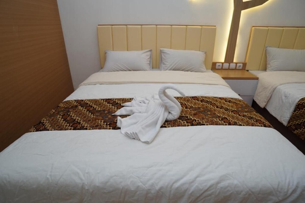Quarto de hotel com duas camas, cabeceiras, mesas de cabeceira e uma toalha no chão.