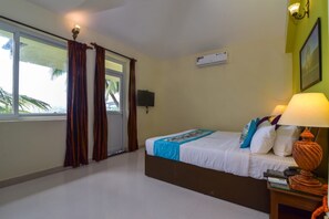 Habitación de hotel con cama, mesita de noche, lámpara, televisor y ventana con cortinas.