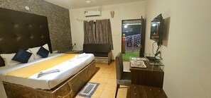 Habitación de hotel con cama, escritorio, televisor y vistas al exterior.