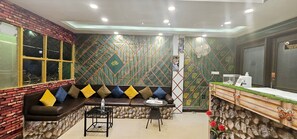 Un área de recepción con pared de piedra, mostrador de madera y zona de estar con cojines.