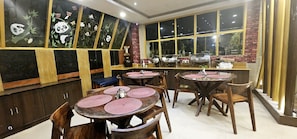 Interior de restaurante con mesas redondas, sillas y una pared decorada con ilustraciones de pandas.