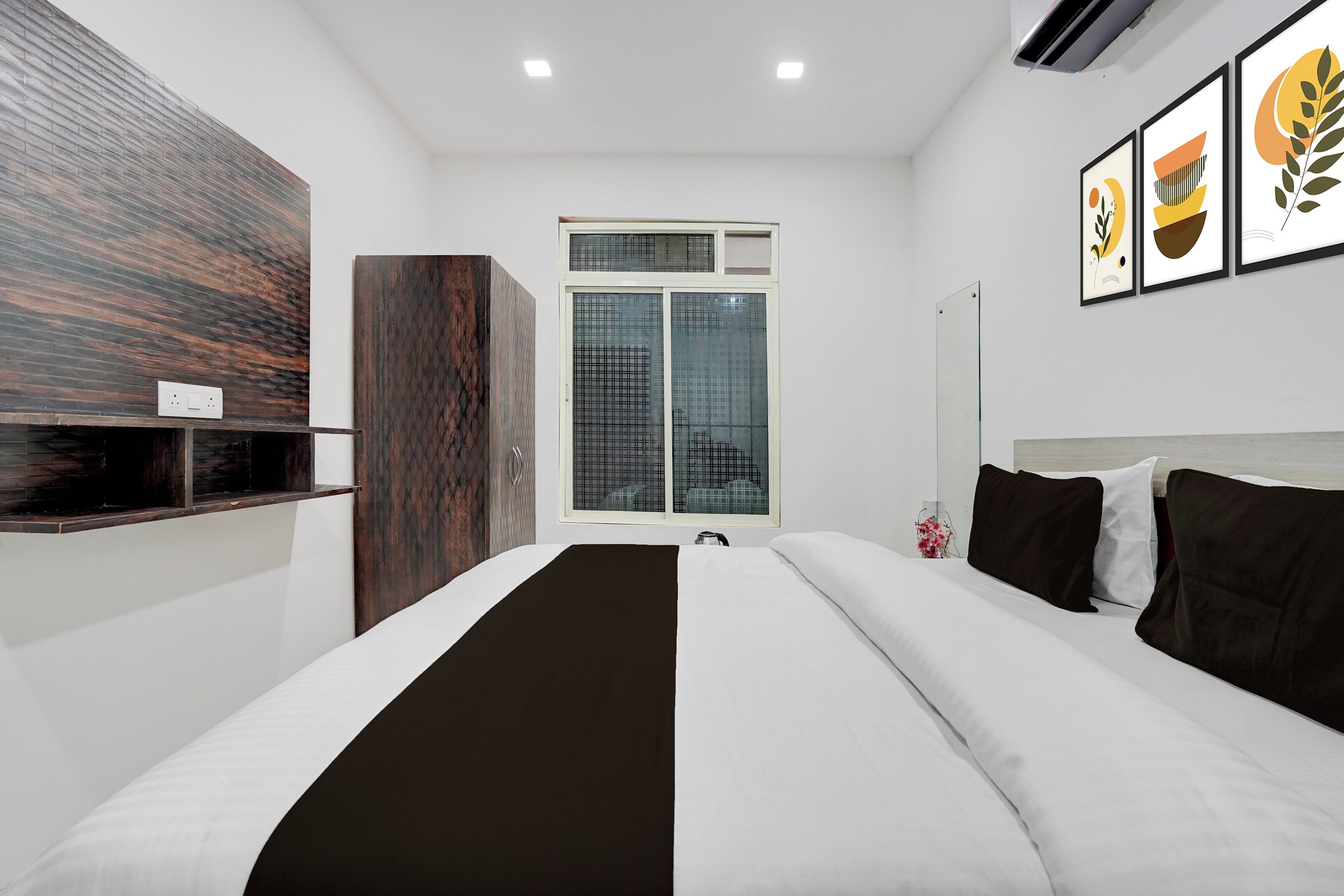 Une chambre d’hôtel moderne avec un grand lit, un mur décoratif en bois, une fenêtre donnant sur un immeuble et des œuvres d’art accrochées au mur.