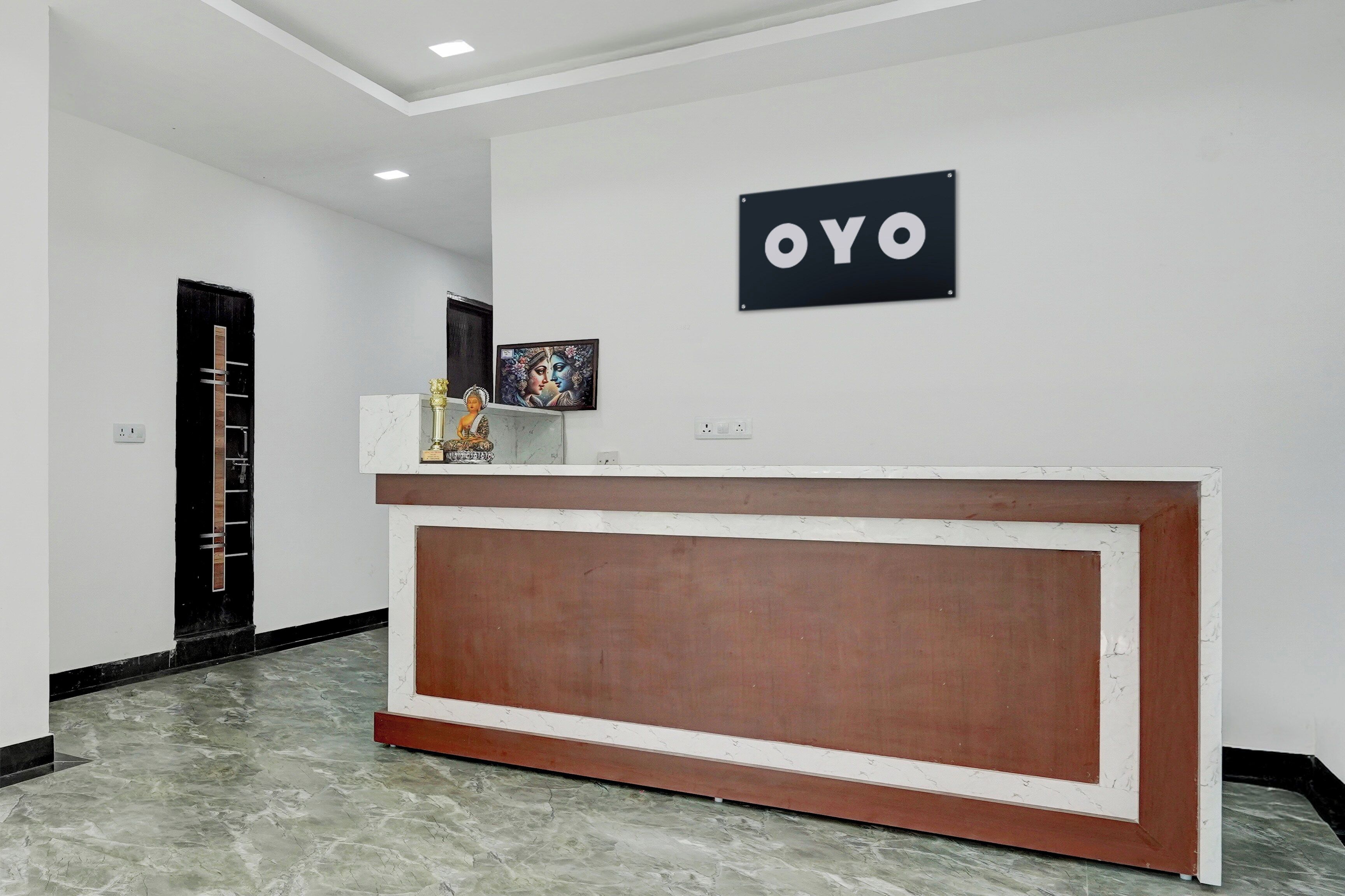A reception area with a marble reception desk, a black sign with 'OYO' on the wall, and a framed artwork above the desk.