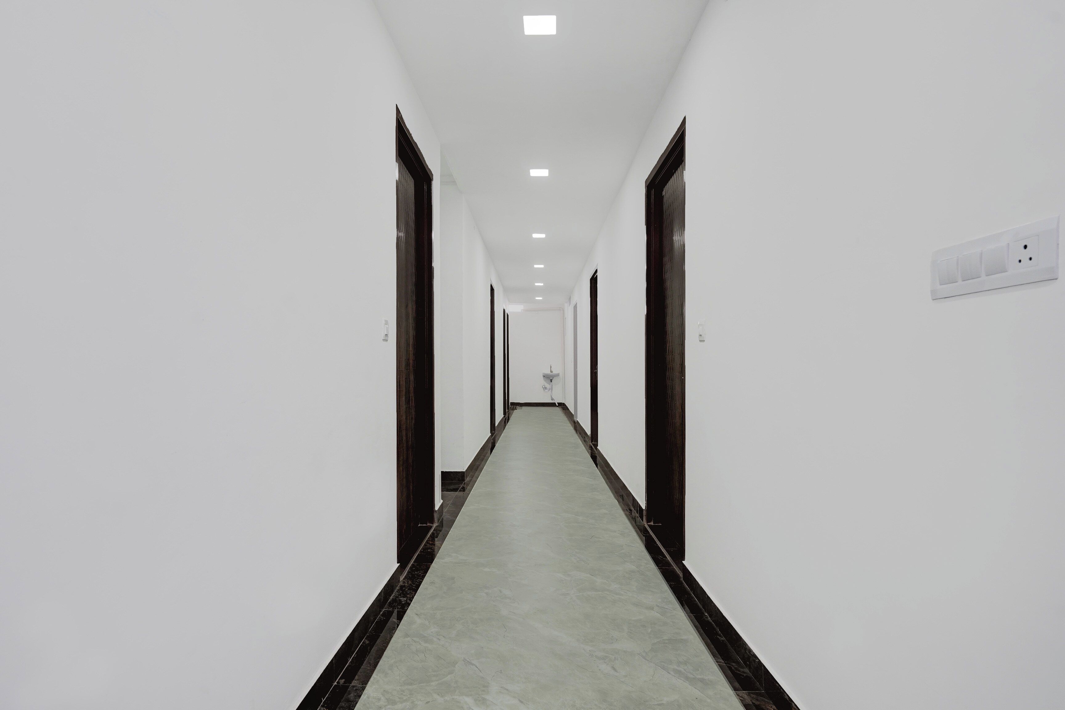 A long, narrow hallway with white walls, dark wooden doors, and a light-colored floor.