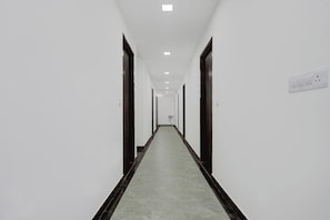 A long, narrow hallway with white walls, dark wooden doors, and a light-colored floor. - Hotel O The King Heaven (Farrukhabad)