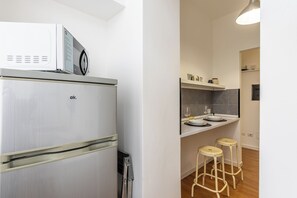 A compact kitchen with a refrigerator, a microwave, and a small countertop with stools. - New Listing (Lecco)