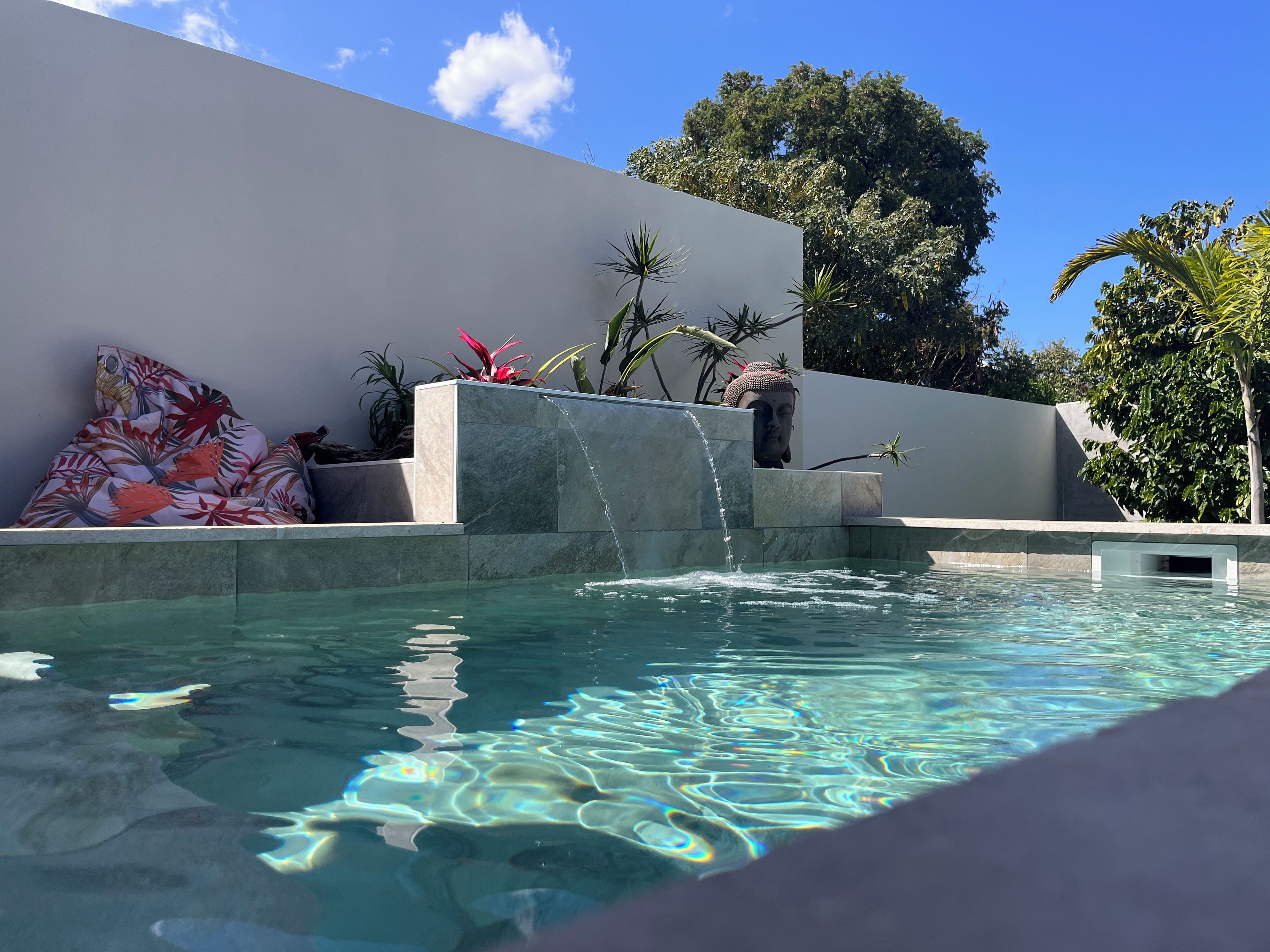 A pool with clear water, a waterfall feature, and a Buddha statue.