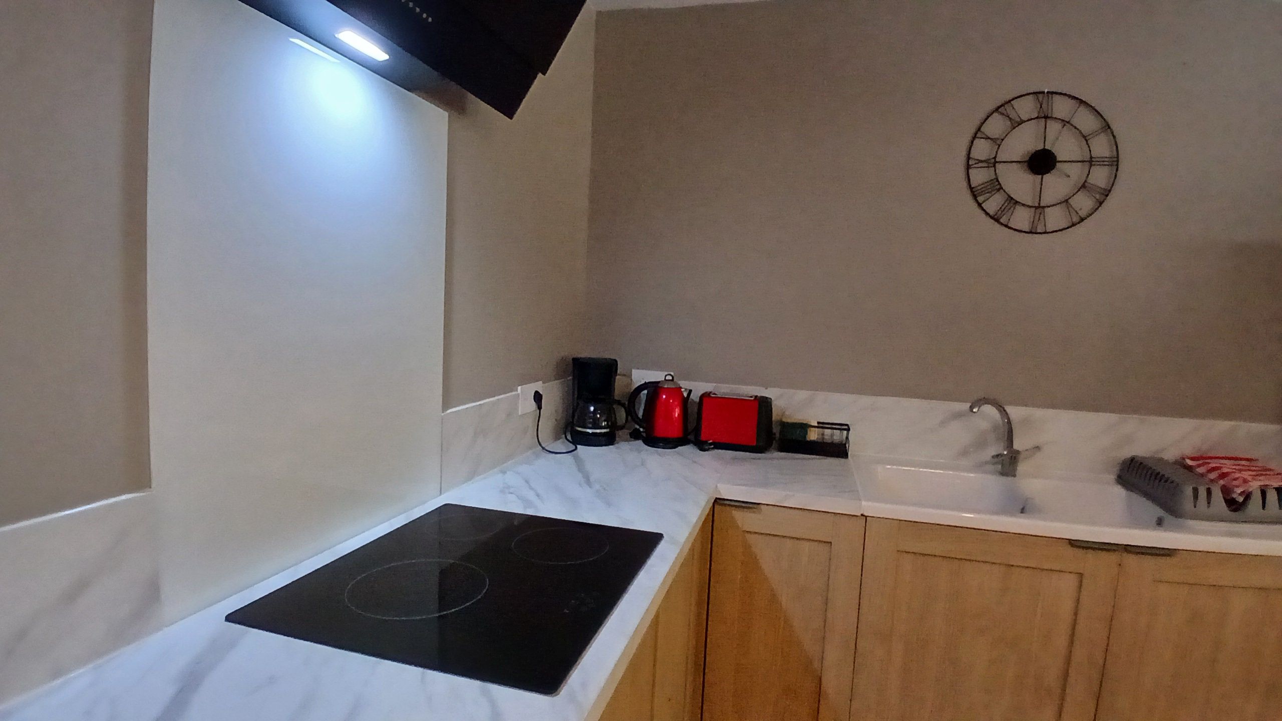 Een keuken met een zwart inductiefornuis, een koffiezetapparaat, een broodrooster en een klok aan de muur.