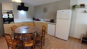 Eine kleine Küche mit einem runden Esstisch, Holzstühlen, einem weißen Kühlschrank und einer Uhr an der Wand.