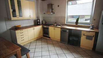Een keuken met een houten plafond, gele kastjes, een raam en een betegelde vloer.