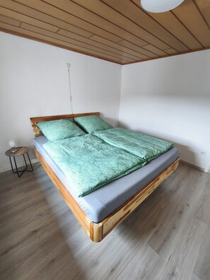 A single bed with a wooden frame and a green patterned bedspread.