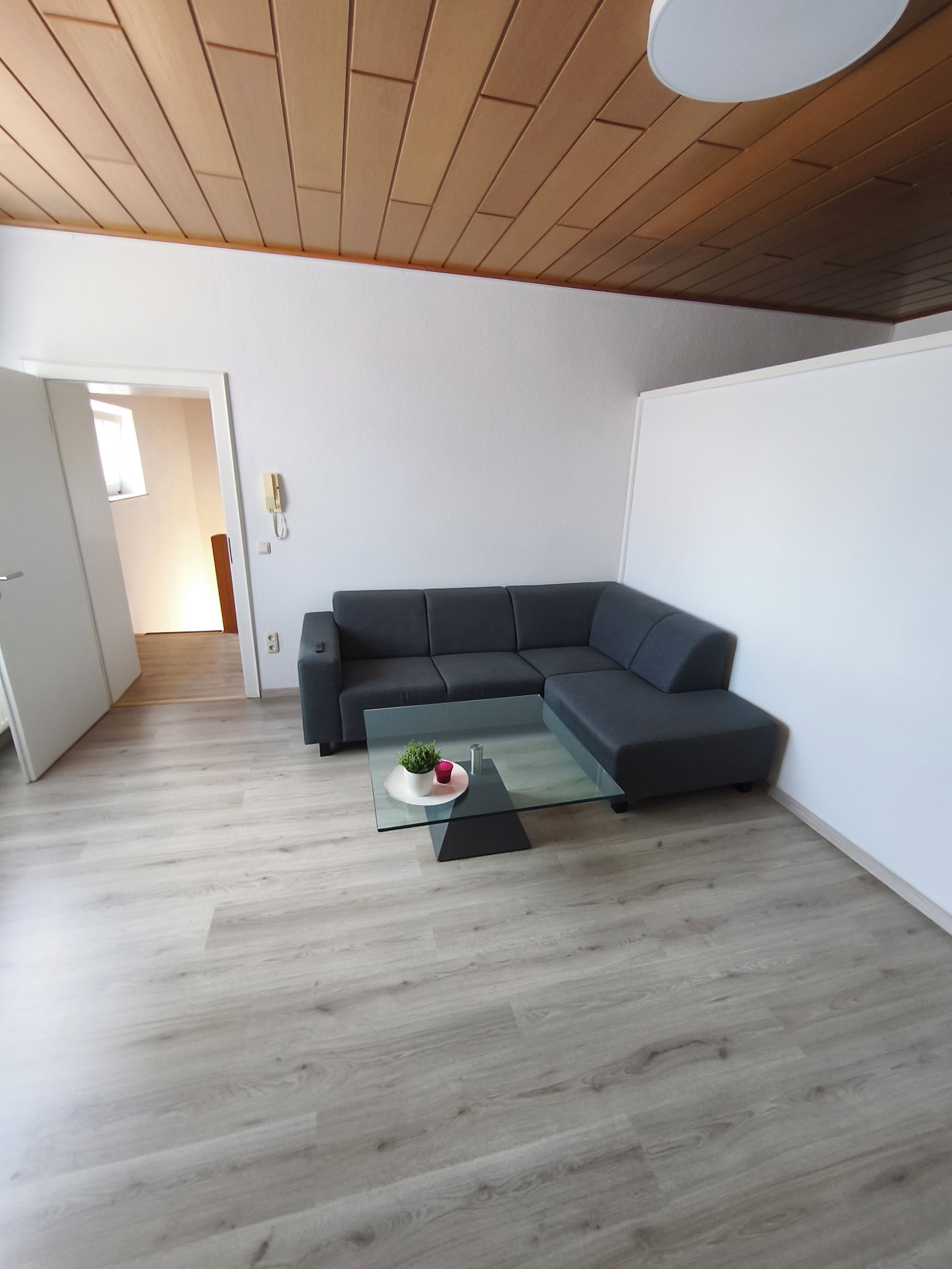 Een moderne woonkamer met een hoekbank, een glazen salontafel en een houten plafond.