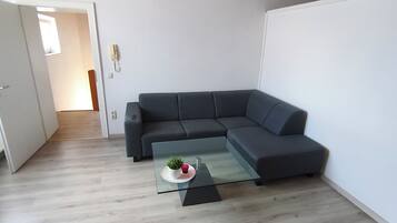 Een moderne woonkamer met een hoekbank, een glazen salontafel en een houten plafond.