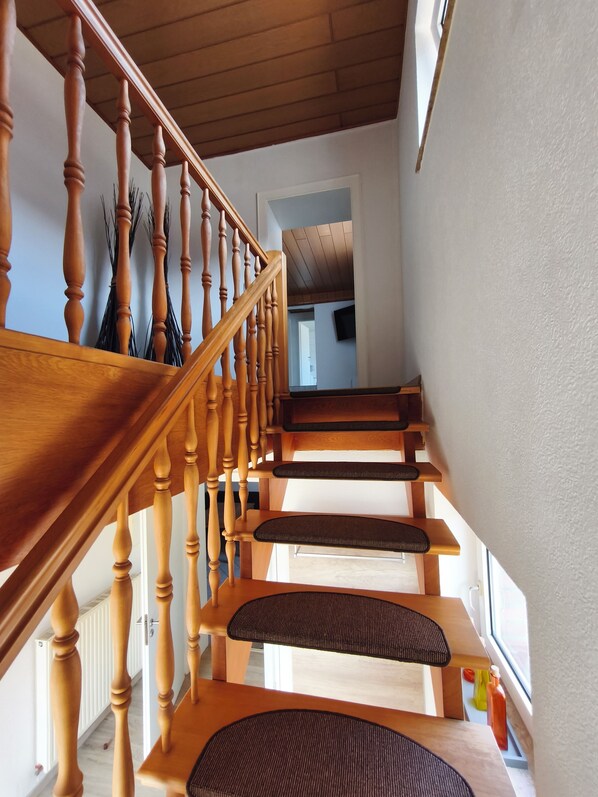 A wooden staircase with a handrail and a landing area with a bench.