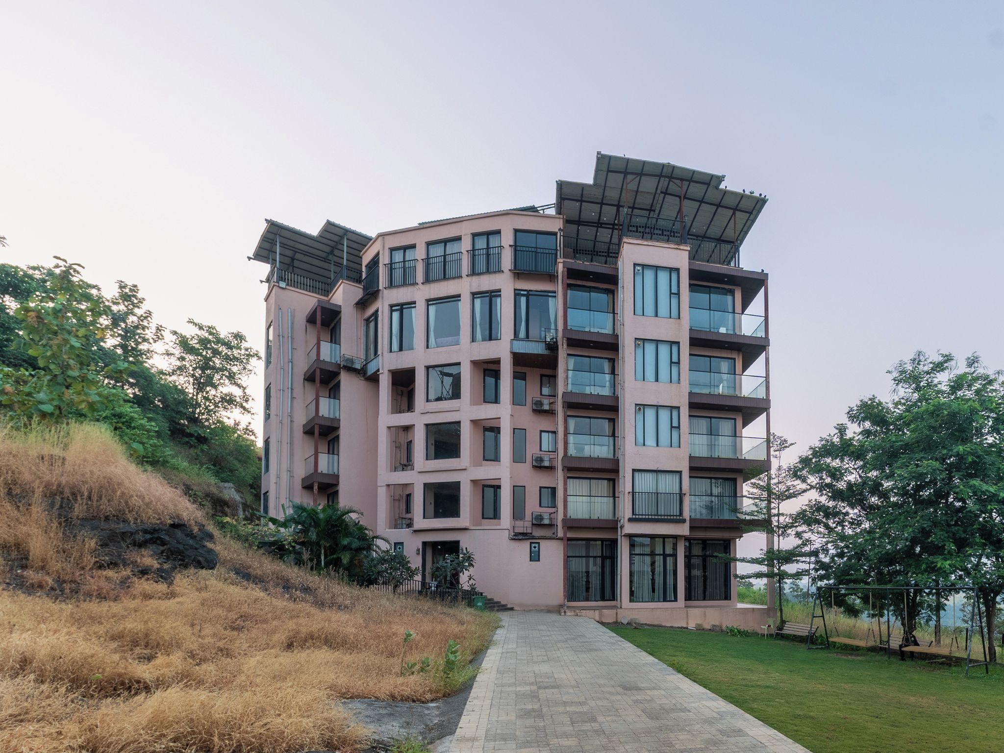 Un edificio residencial de varios pisos con balcones, un sendero pavimentado y vegetación circundante.