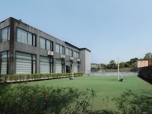A building with large windows and air conditioning units, a green lawn, and a stone wall. - Paraiso Club & Resort (Igatpuri)