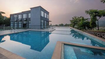 Un edificio moderno con un área de piscina, que incluye una piscina rectangular y una sección más pequeña con borde de azulejos.
