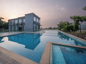 Un edificio moderno con un área de piscina, que incluye una piscina rectangular y una sección más pequeña con borde de azulejos.