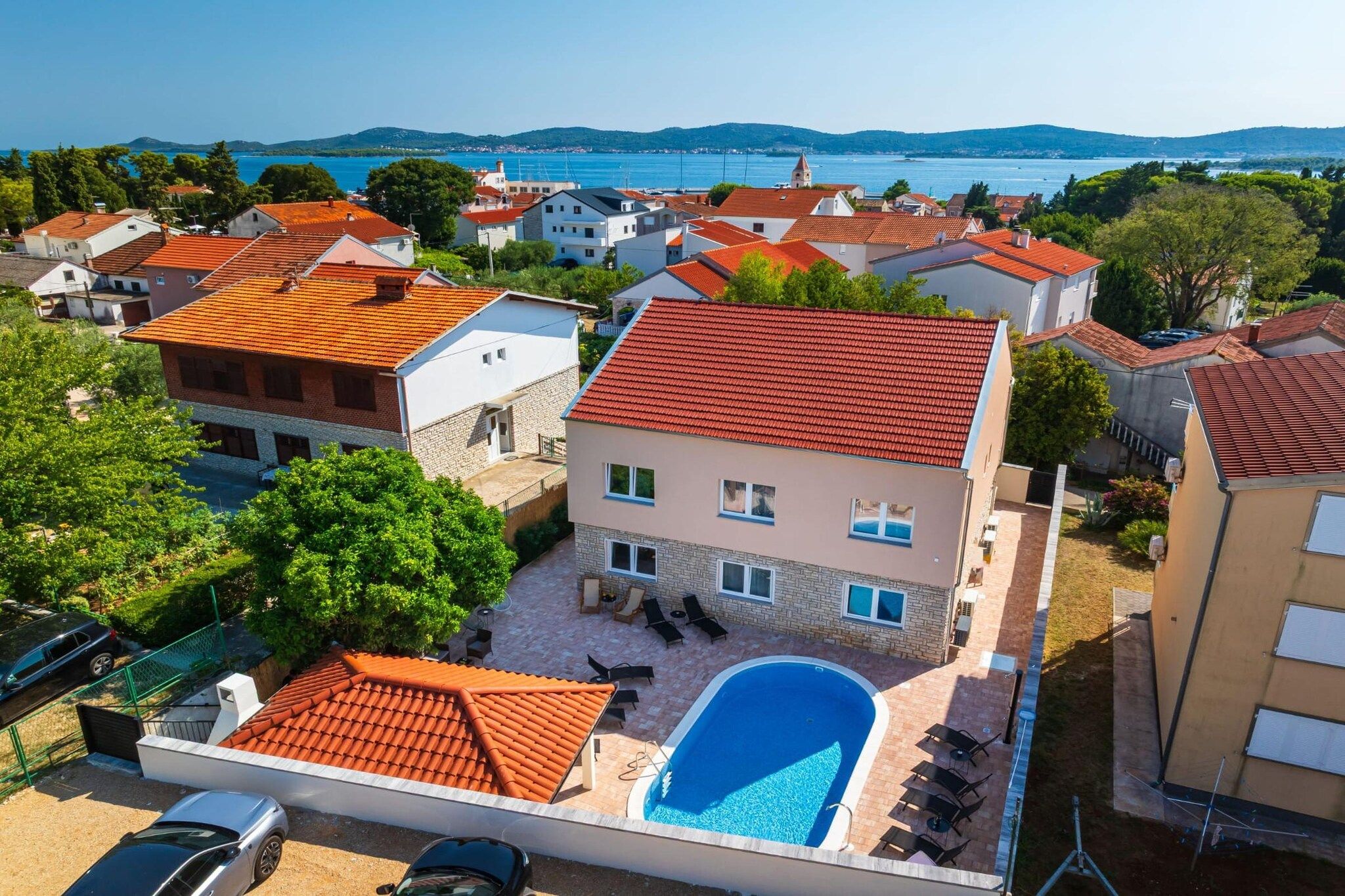 A residential area with a swimming pool, multiple houses, and a view of the sea.