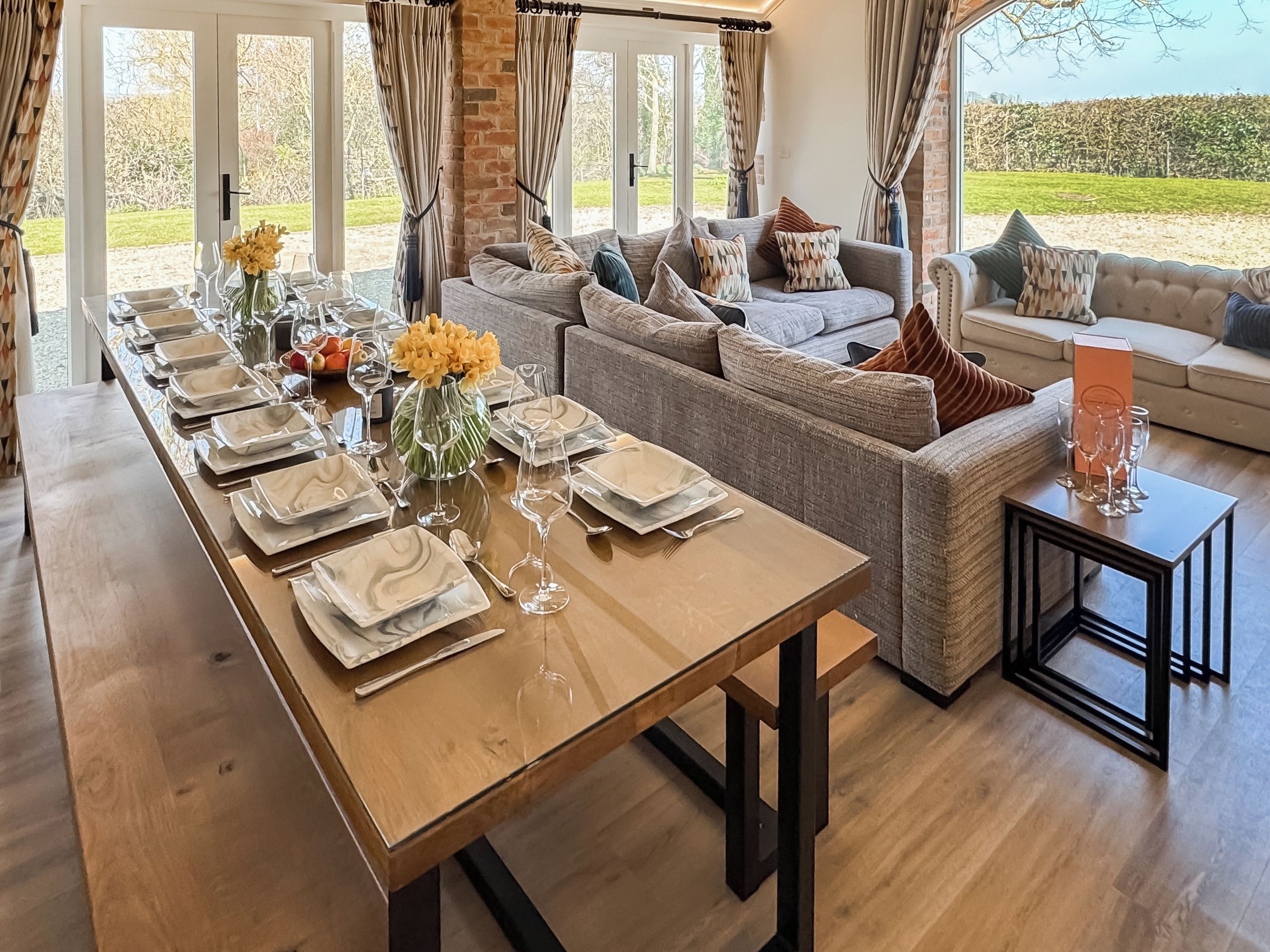 A dining area with a long table set for a meal, a sofa, and a view of the outdoors.